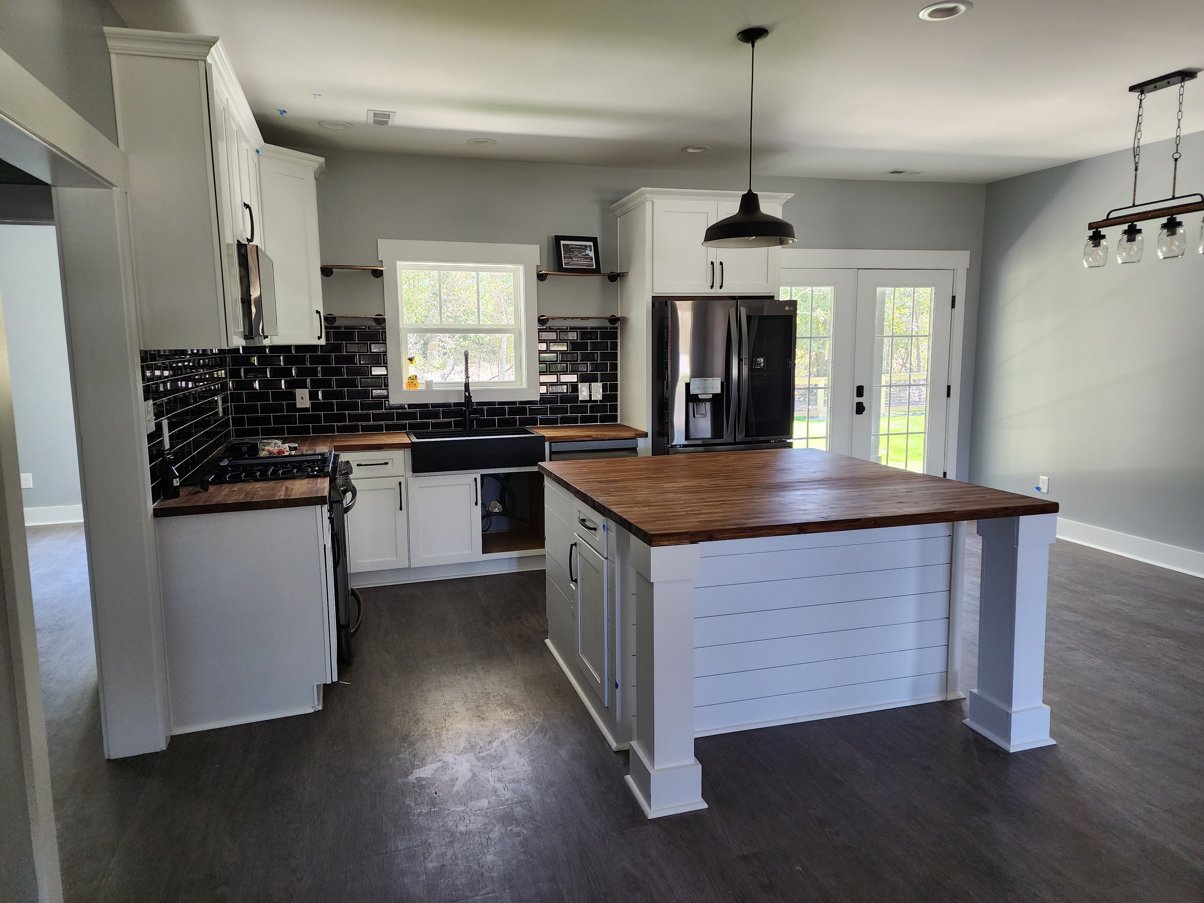 Completed kitchen with white cabinets, dark tiles, and wooden island top