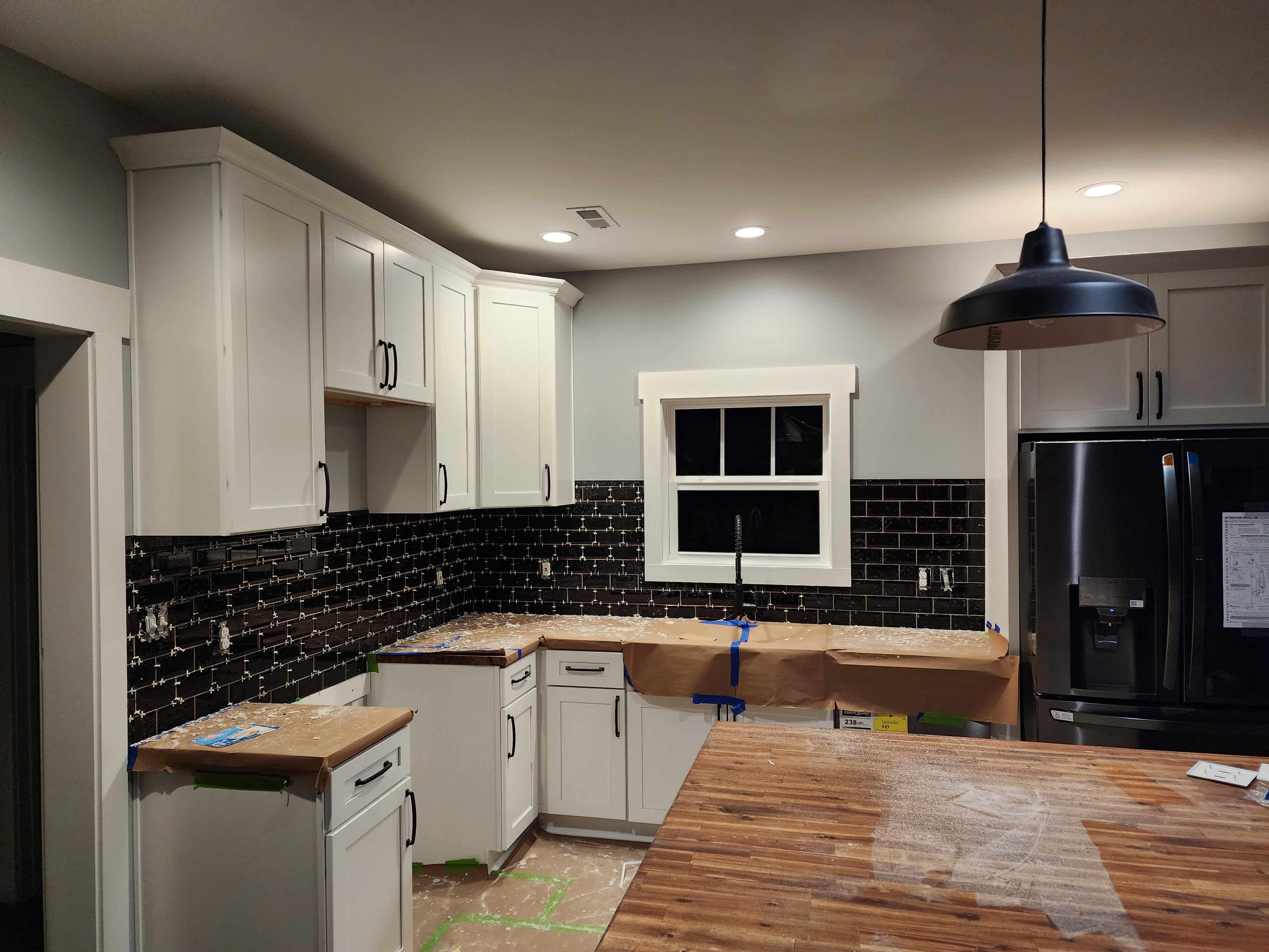 Kitchen during renovation with white cabinets and dark tile backsplash installation